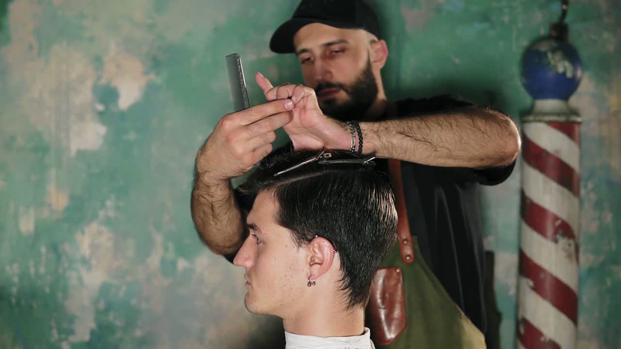 Bearded barber putting hair pins to man's head and brushing his hair. Hair barrette on male head in barber shot. Male hairstyle