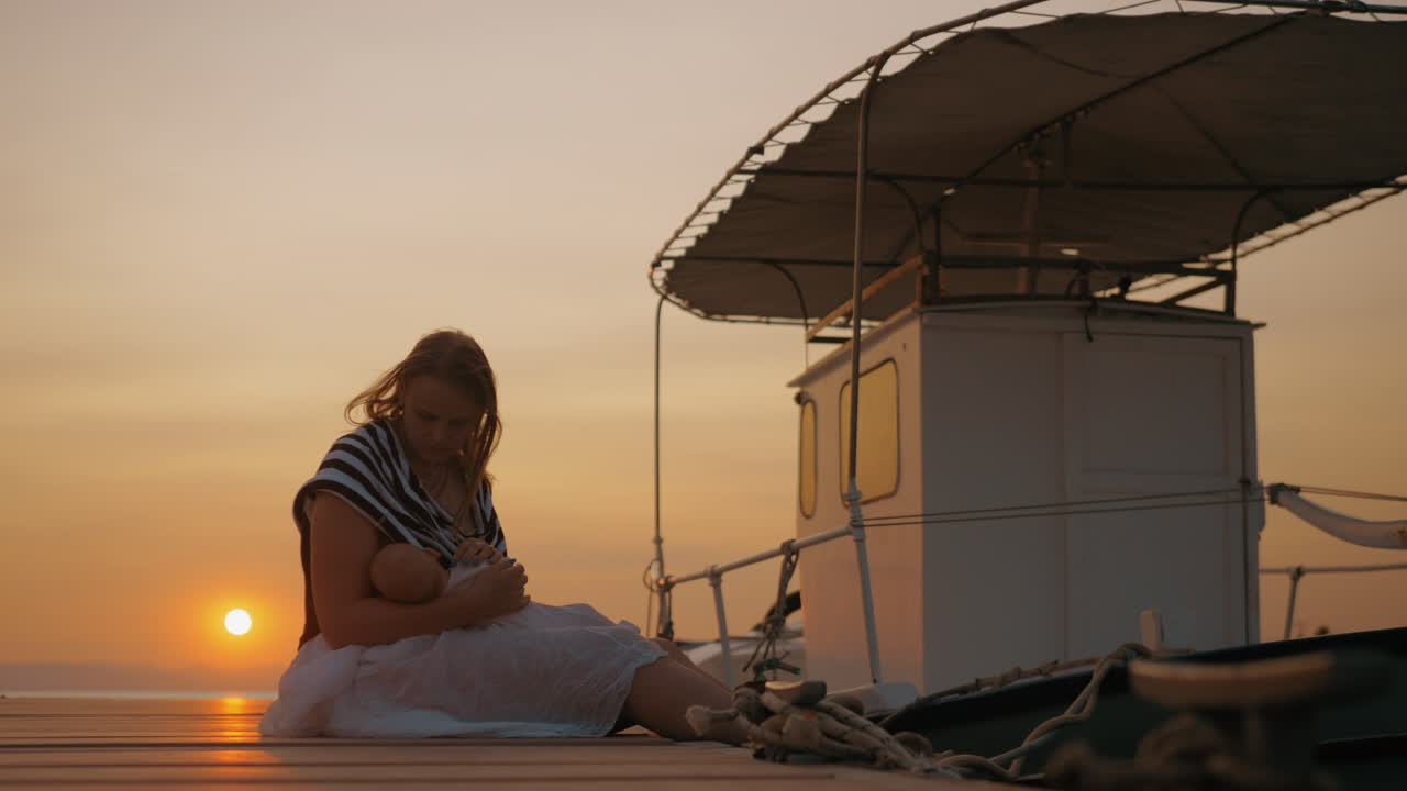 Madre che allatta il bambino sul molo al tramonto