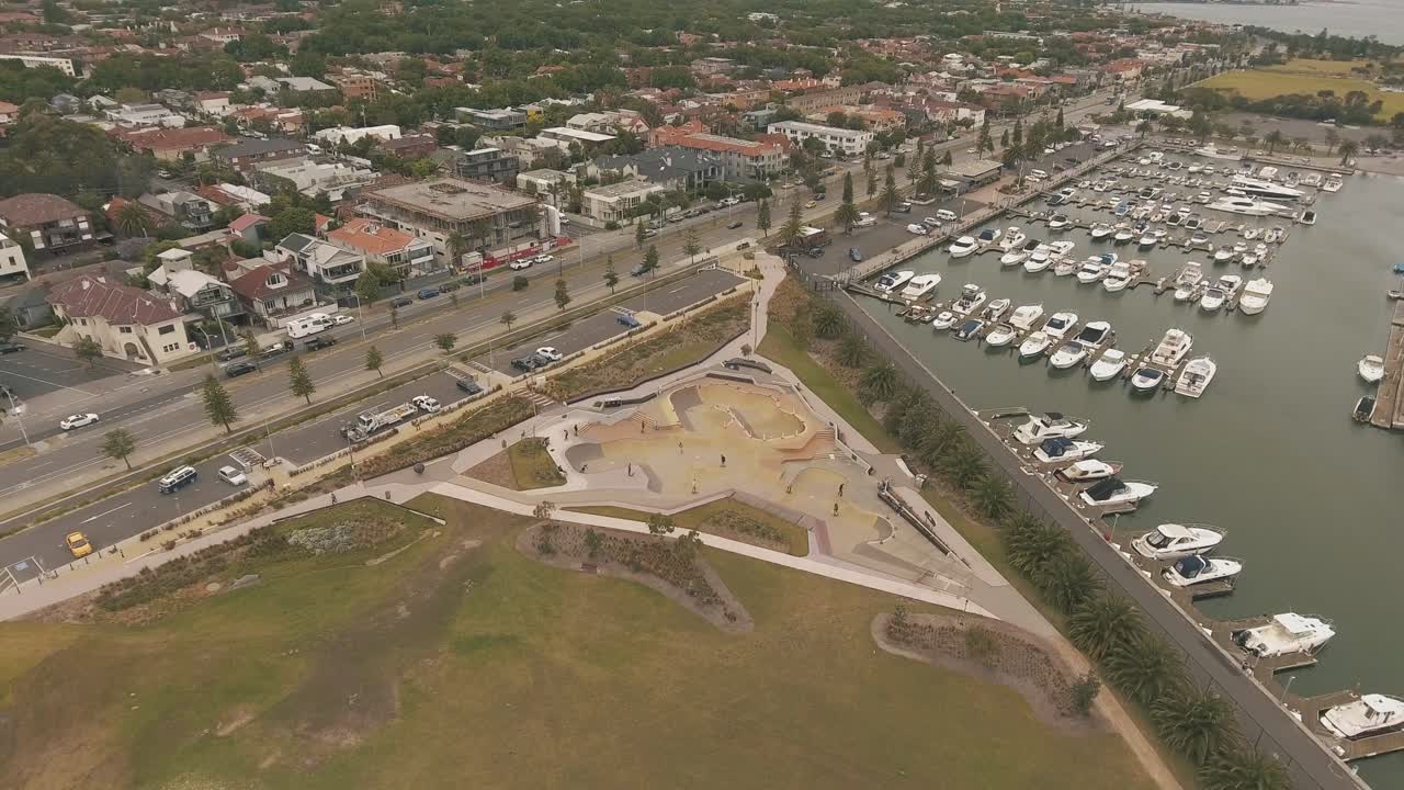 부두에 보트가 있는 흐린 날에 세인트 킬다의 물 옆 스케이트 공원 위에 드론 공중