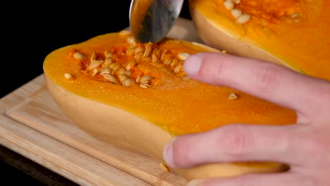 locked off view of seeds being scooped out of butternut pumpkin with metal spoon