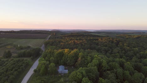 Luftaufnahme-Eines-Im-Wald-Versteckten-Sommerhauses-In-Der-Nähe-Der-Malerischen-M22--Und-Sleeping-Bear-Dünen-Und-Der-Durchquerung-Der-Stadt-Michigan-Bei-Sonnenuntergang,-Während-Das-Licht-Die-Wipfel-Der-Bäume-Küsst