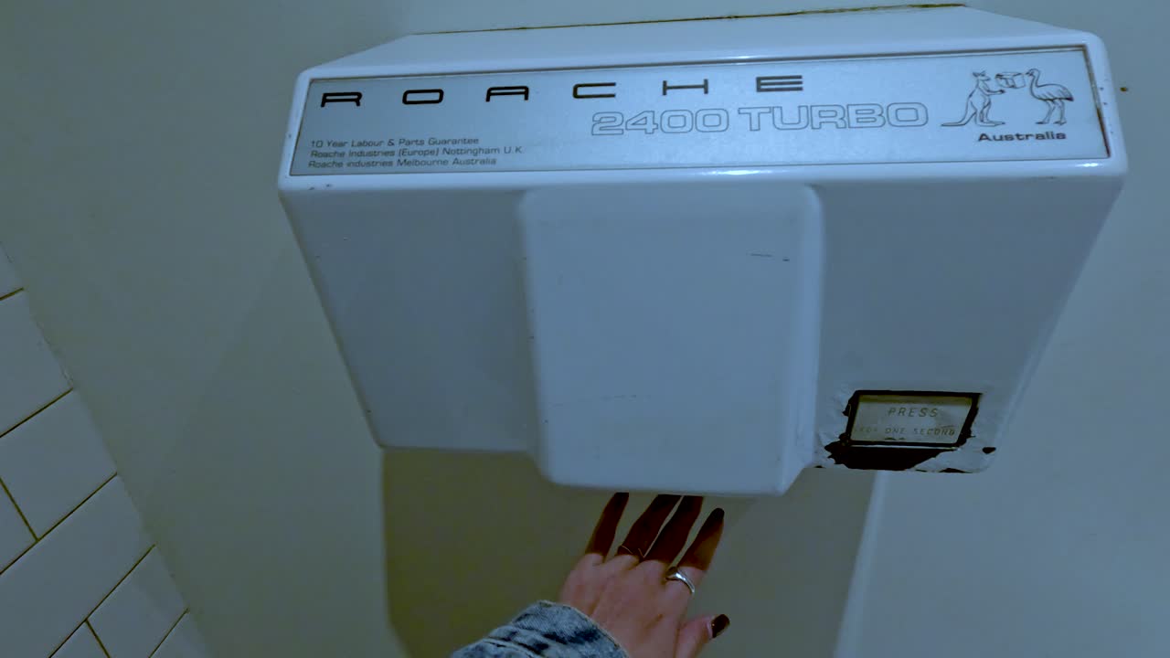 한 사람이 타일로 된 화장실에서 벽에 장착된 손 건조기를 사용합니다.