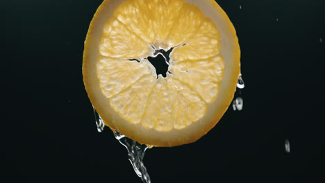 water flowing down fresh orange slice in slow motion with backlit black background