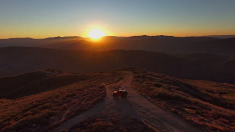 man on top of overlanding jeep roof in middle of desert mountain at sunset