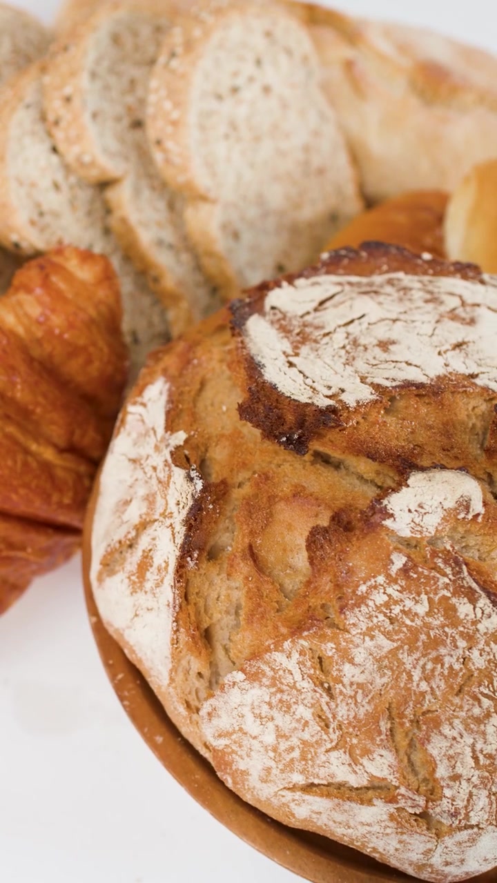 Close-up of rotating sourdough bread, croissants, and sliced baguette on a white background.