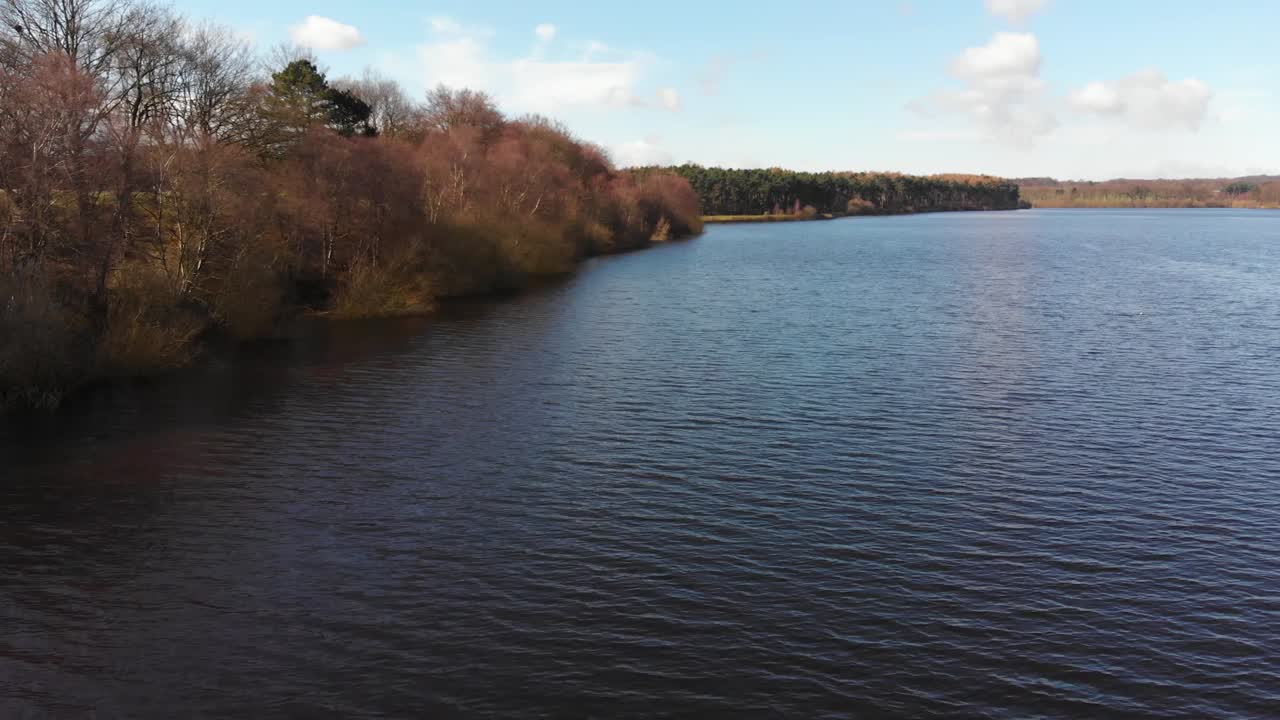 Plan de drone aérien survolant un lac calme dans la campagne anglaise par une journée d'été, révélant un paysage isolé.