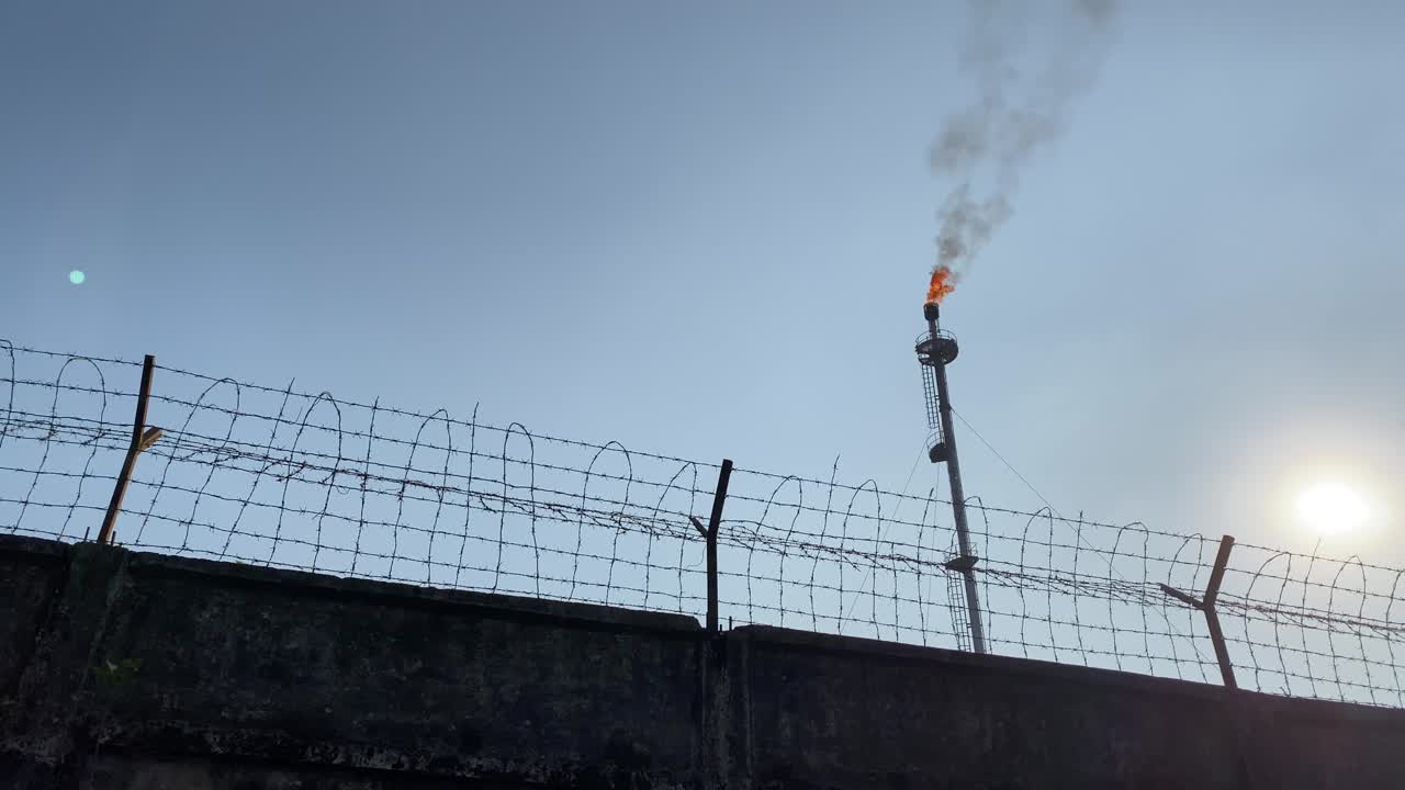 가스 플레어가 맑은 하늘에 타오르는 낮은 각도의 유선 벽, 낮