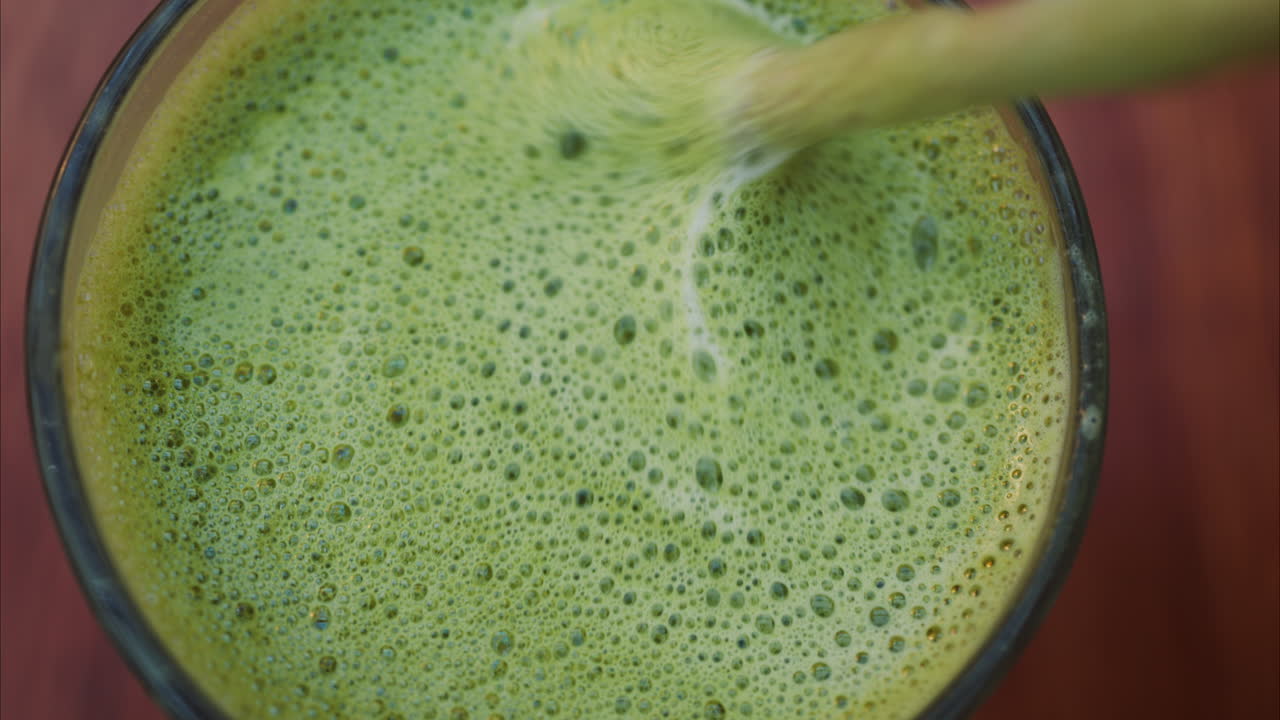 Close up of a woman mixing a matcha latte with a paper straw at a cafe