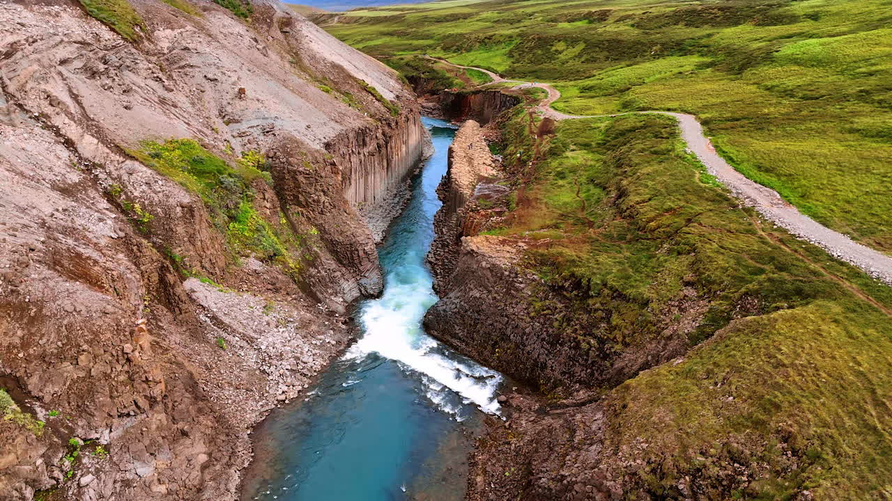 River flowing in the crack in the mountains. Top view on the rocks covered with green moss. Iceland wild nature.