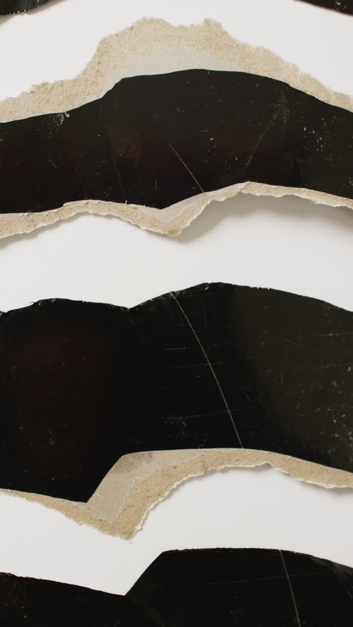 Vertical video of close up of torn pieces of black paper to white background with copy space