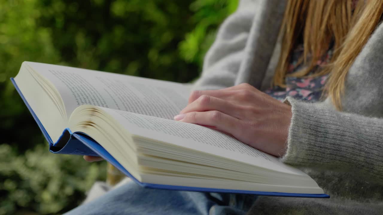 Female hand flips book page while reading outside, slow motion,