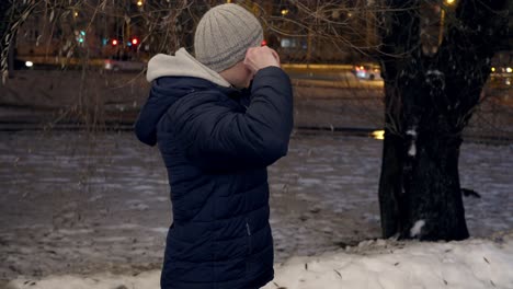 Caucasian-man-with-blue-jacket-puts-on-a-hat-outdoors-in-cold-winter-evening