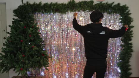 joven colocando luces de navidad decoración en estudio con árbol de navidad