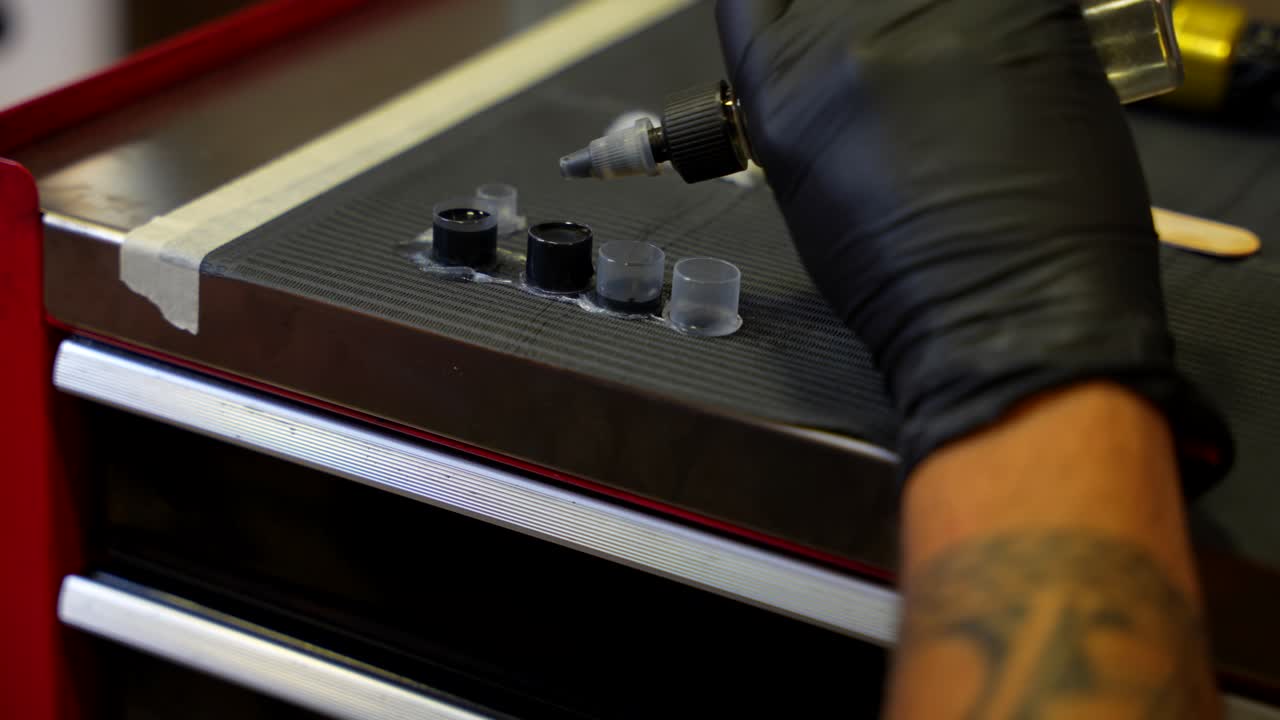 Close-up of a tattoo artist’s hand adding a few drops of distilled water to a small ink pot. Slowmo