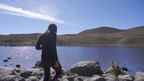 woman holding camera and standing on top of the rock in nature