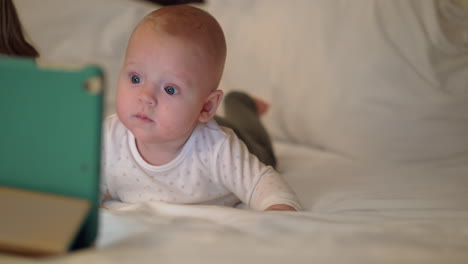 cute baby girl lying on a bed and watching on tablet screen