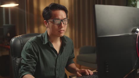 asian male drinking coffee while works on his personal computer with big display, he works at night