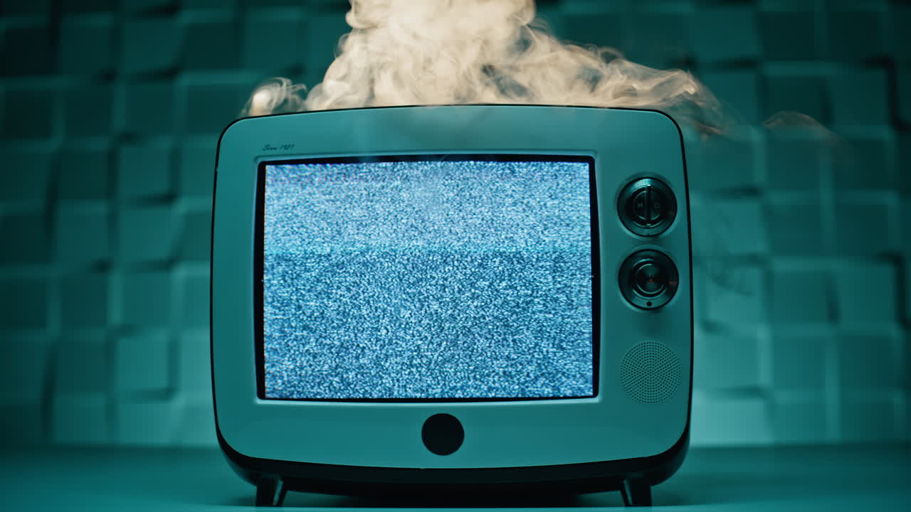 Primo piano di un televisore rotto con monitor lampeggiante appoggiato su un tavolo in un appartamento. Fumo grigio.
