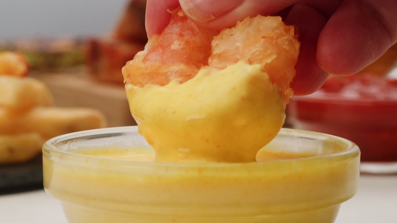 Hand dipping fried shrimp into a sauce