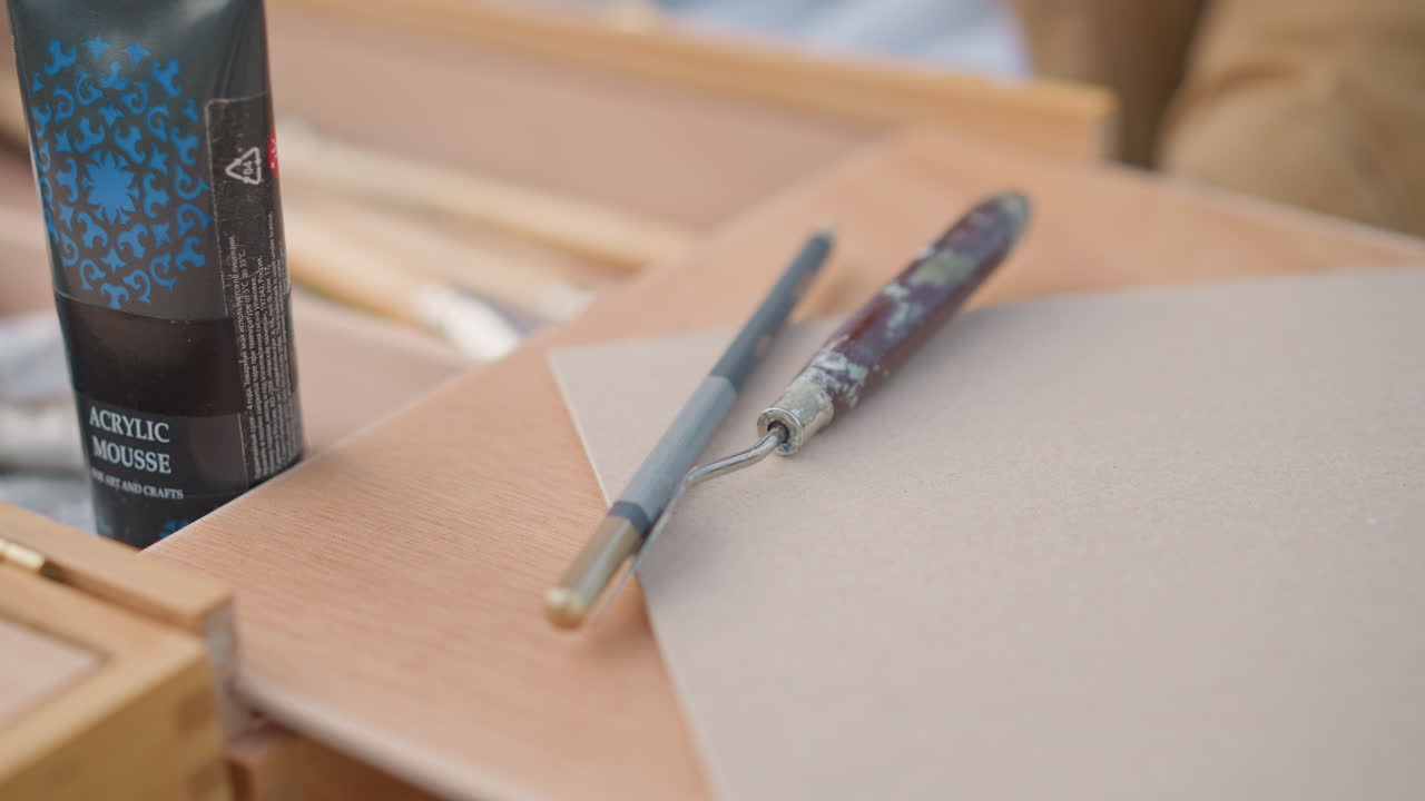 tubetti di pittura, pennelli su cavalletto di legno, artista di strada che dipinge all'aria aperta, intento a preparare palette e aree di lavoro, primo piano di barattoli e pennelli all'interno di una scatola di legno, carta ruvida per schizzi, luce naturale soffusa, colore neutro