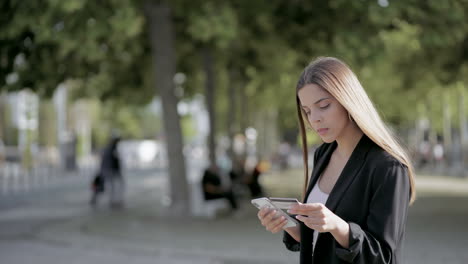 chica seria con tarjeta de crédito usando teléfono inteligente al aire libre