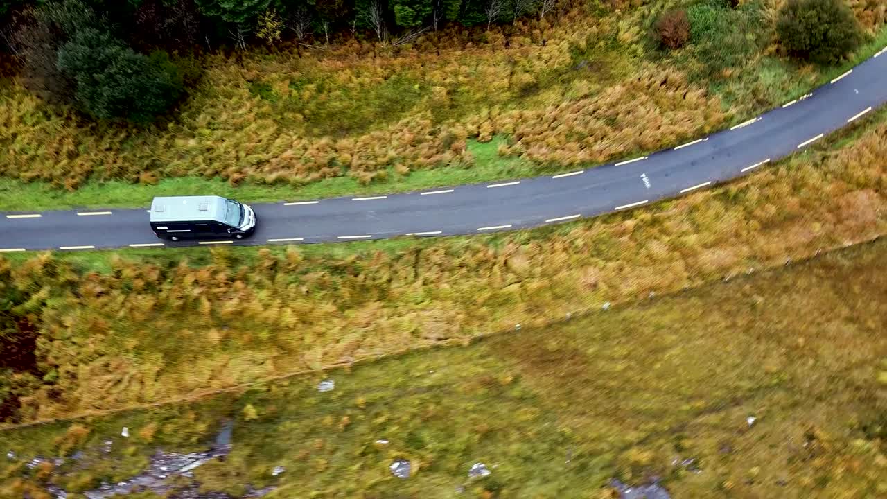 İrlanda'da manzaralı bir köy yolunda yolculuk yapan bir karavanın üzerinde dron kamerasıyla dönerek alçalan görüntüler