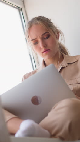 young accountant woman makes calculations for work sitting on windowsill behind brown curtain leaned on pillow at home slow motion