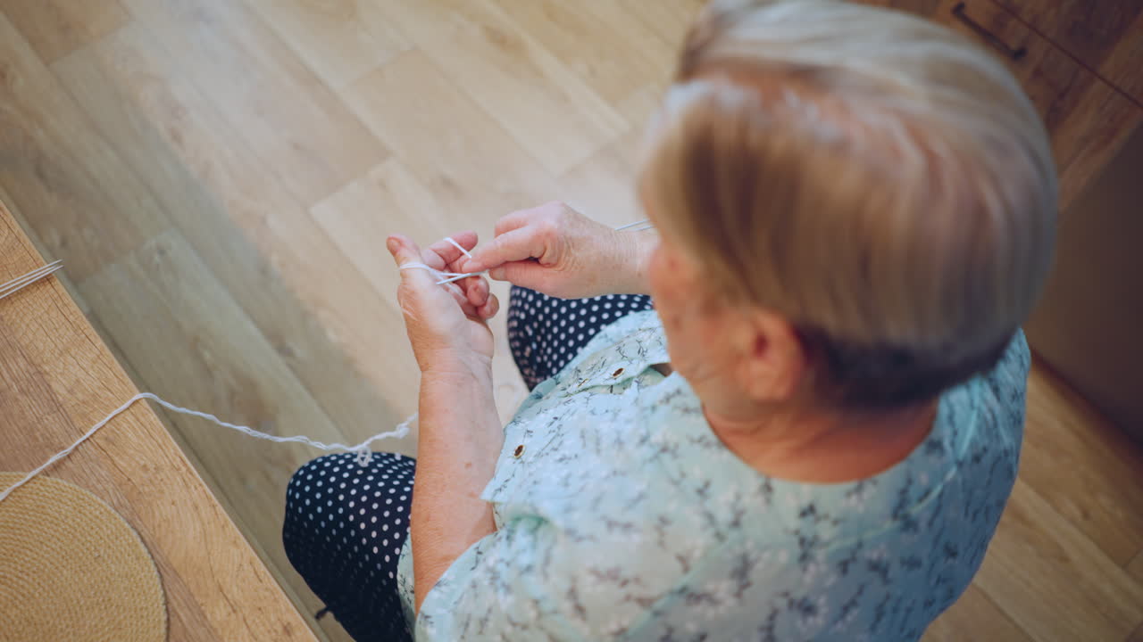 Overhead view grandma crocheting yarn, seated on wooden floor in polka blouse, closeup on hands and thread, warm sunlight, calm domestic atmosphere, tactile tradition and memory, patient craft therapy