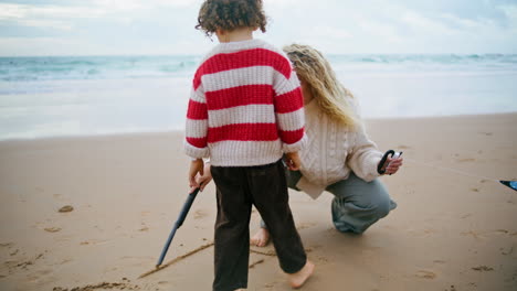 Madre-Hijo-Dibujando-Playa-Con-Palos-El-Fin-De-Semana-De-Otoño.-Familia-Jugando-Junto-Al-Mar