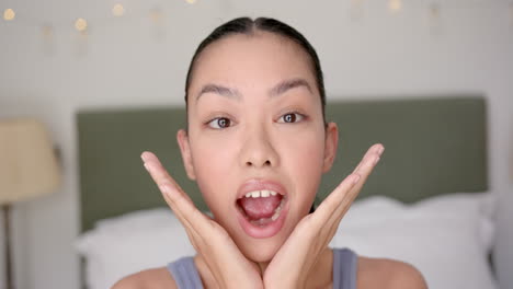 young biracial woman with her eyes closed, hands framing her face in a bedroom