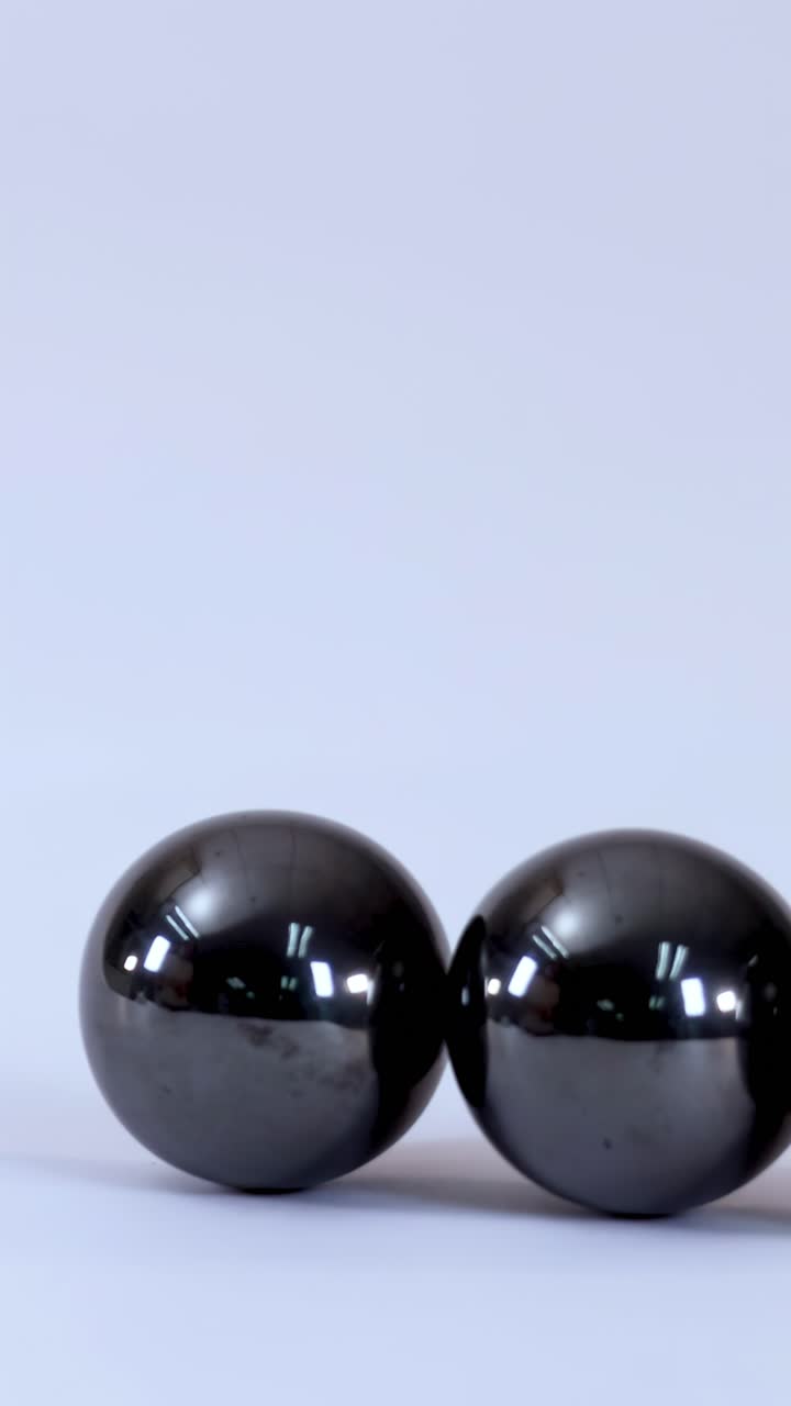 Close-up shot of three metallic magnetic balls rotating and rolling across a plain white background