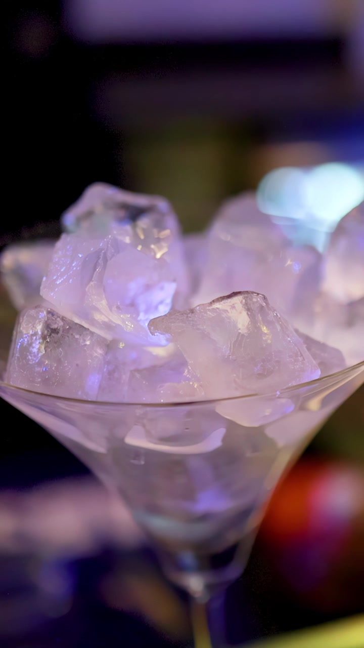 Bicchiere da Martini con cubetti di ghiaccio su bancone da bar, illuminazione al neon vivace, profondità di campo ridotta