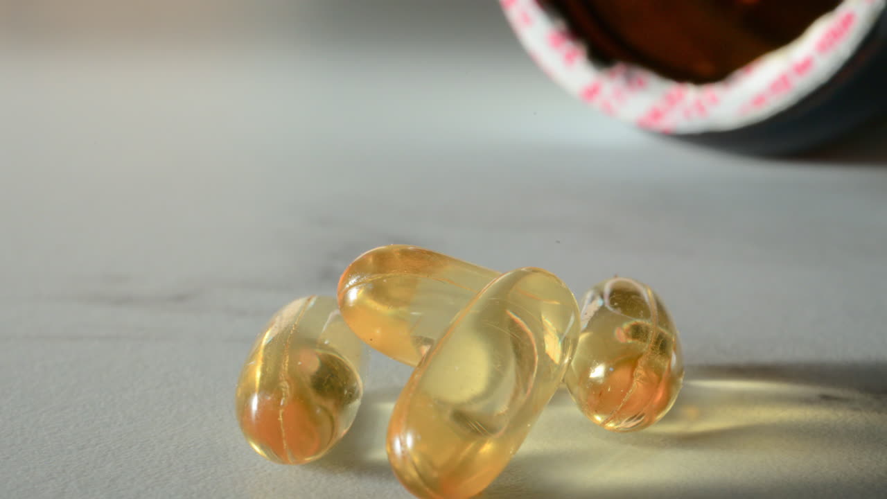 Close up of fish oil supplements scattered on a white table near a pill bottle