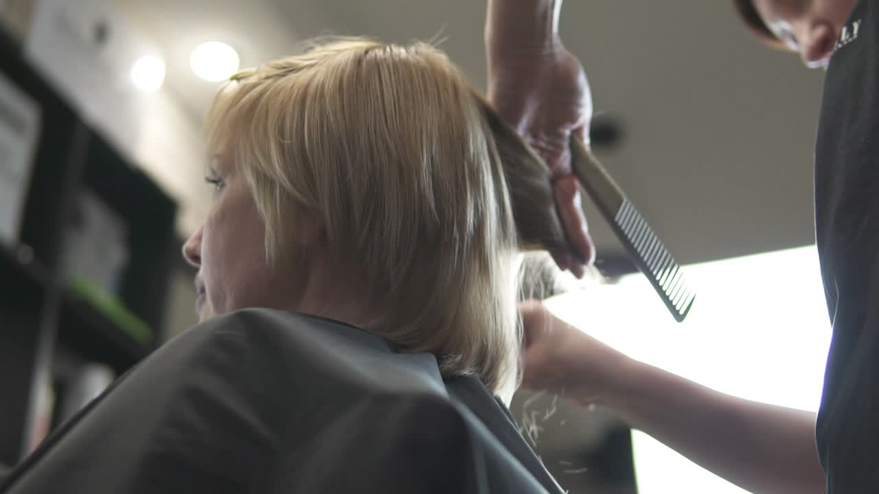 Young woman getting her hair dressed in hair salon. Close Up view of a hairdresser's hands cutting hair with scissors. shot in