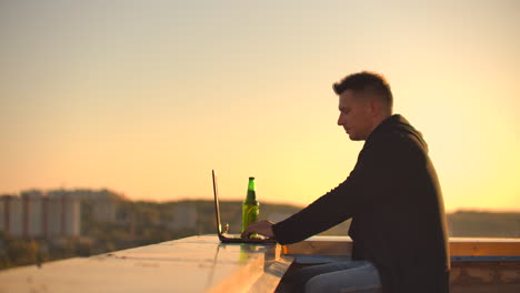 Hipster-man-with-a-laptop-on-the-edge-of-the-roof.-Freelancer-at-work.-Wireless-mobile-Internet.-He-works-on-the-Internet.