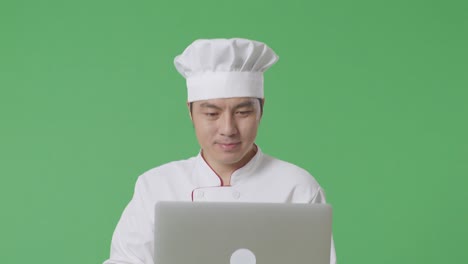 chef asiático usando una computadora portátil mientras camina en el estudio de fondo de la pantalla verde