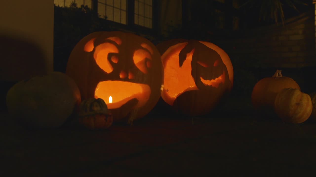 2 carved lit pumpkin outside the front of a house Halloween
