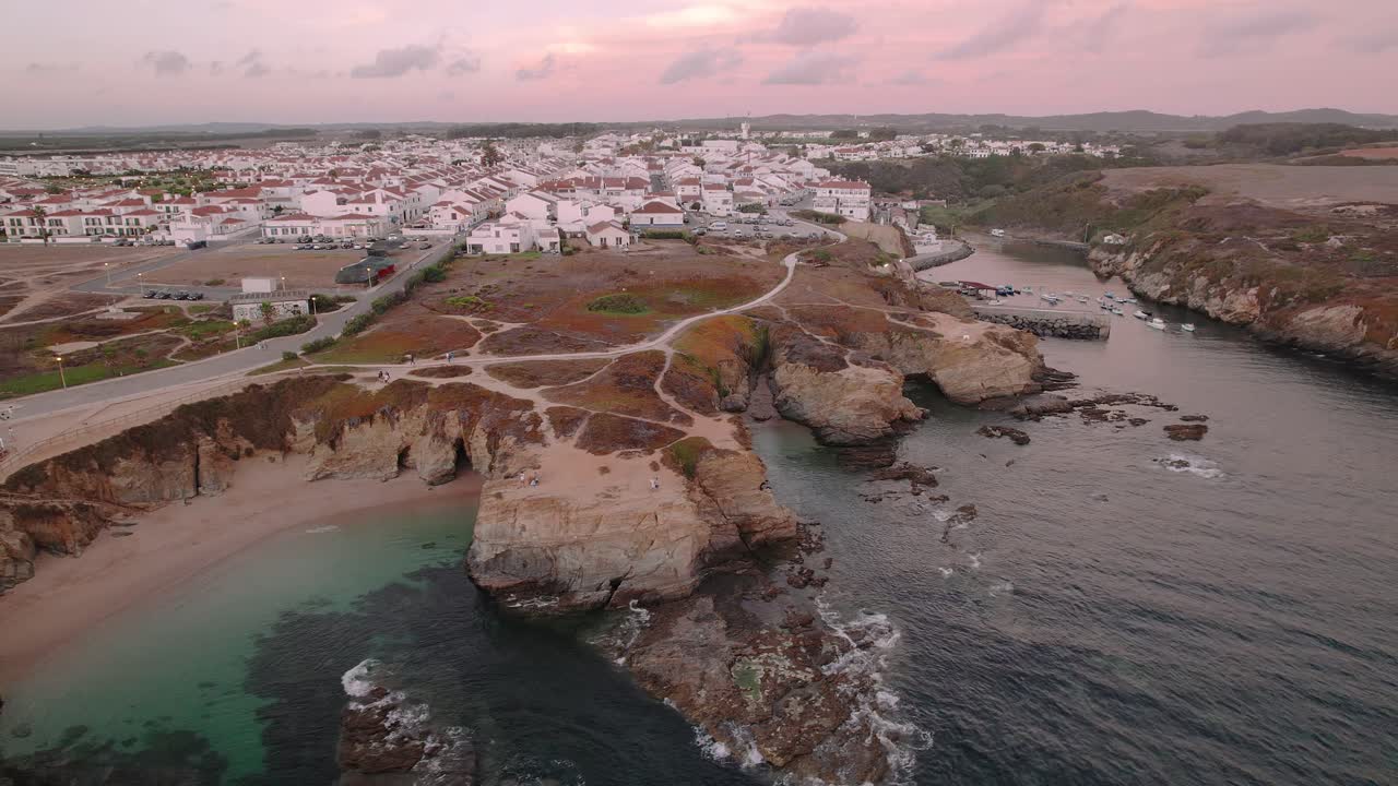 Il villaggio di Porto Covo si affaccia su formazioni rocciose atlantiche scolpite e una baia turchese lungo la Costa Vicentina nell'Alentejo, Portogallo, con drone in orbita.