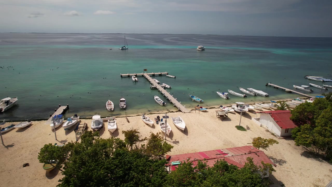 Perairan pirus Gran Roque, dermaga, dan pantai di bawah langit cerah, kepulauan Los Roques, tampilan udara.