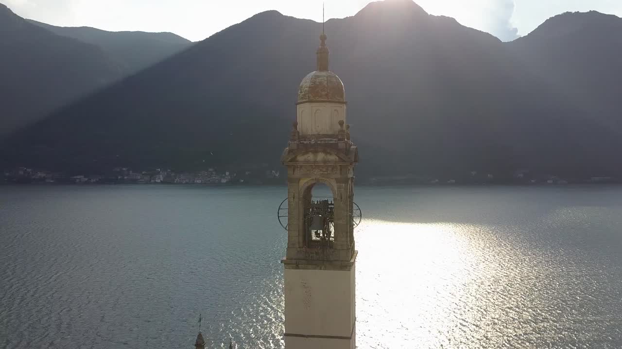 fotografía deslizante de una torre del reloj de la iglesia detrás del lago como con la cordillera, nesso, italia