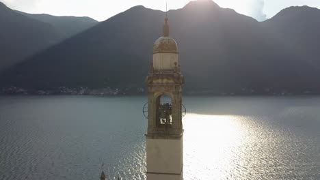 Sliding-shot-of-a-church-clock-tower-behind-Como-lake-with-mountain-range,-Nesso,-Italia