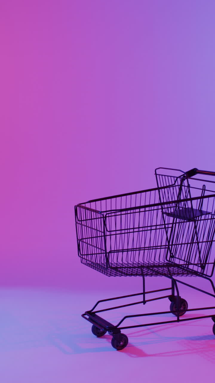 Vertical video of shopping trolley with copy space over pink neon background