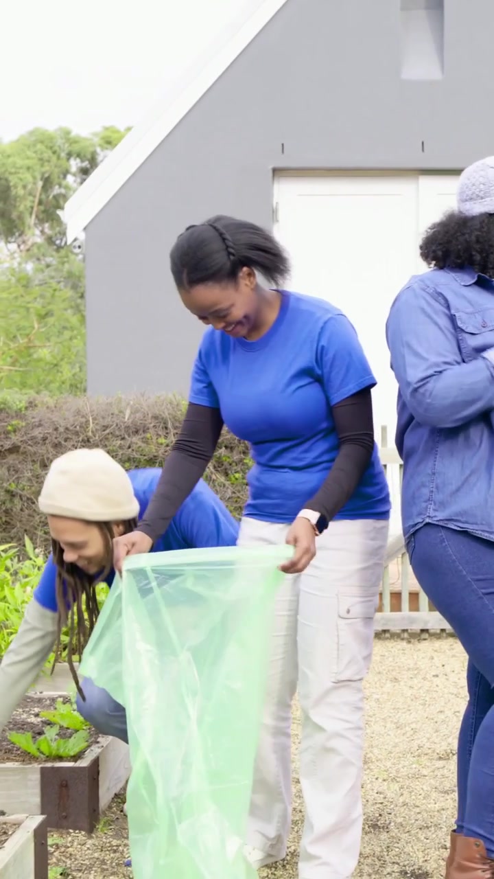 Vertical video: Opening green bags, group in matching blue shirts clearing yard beds for cleanup
