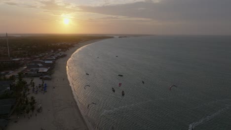 aerial: beach and kiteboarders on the atlantic ocean at sunset with golden hour colors in cajueiro da praia, piaui, brazil, pull out drone shot
