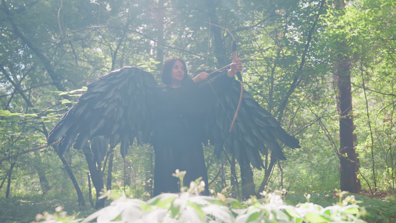 Elegant huntress with black wings draws bow to shoot in sunlit forest, standing poised among green leaves and soft wildflowers, focused gaze, dramatic fantasy mood with backlight glow