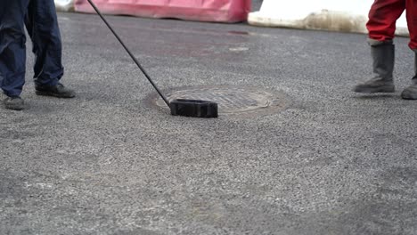 workers pours molten bitumen from a bucket along the manhole after paving new asphalt on the road