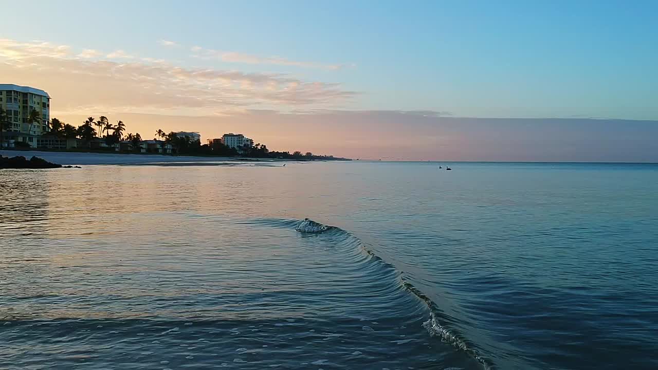volando sobre las olas en la playa de nápoles con un hermoso amanecer y pelícanos en la distancia