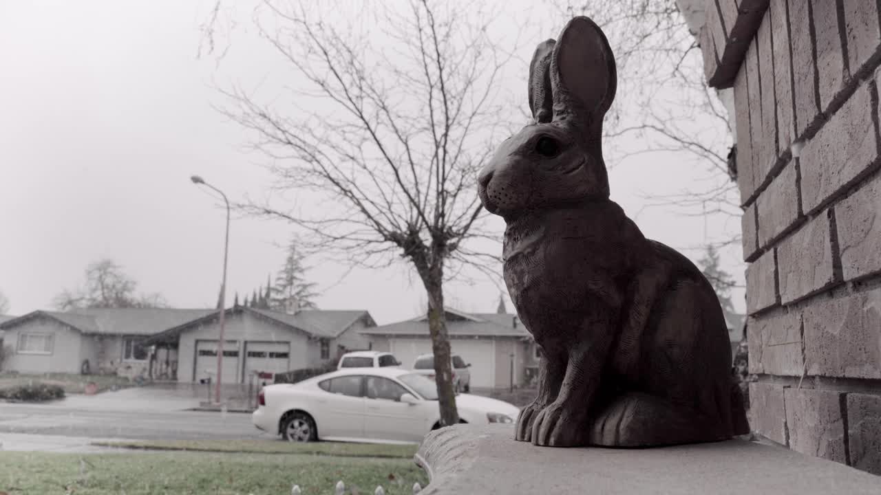 decoración pequeña estatua de conejo en el porche de la casa suburbana durante la fría mañana de invierno con nevadas | 4k
