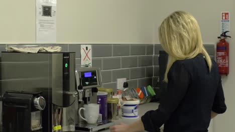 Female-blonde-employee-is-preparing-a-coffee-on-a-coffee-machine-in-a-company-kittchen