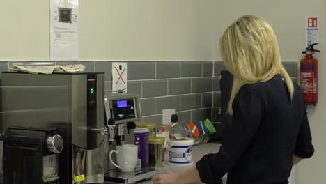 una empleada rubia está preparando un café en una máquina de café en una cocina de la compañía